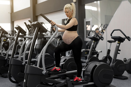 孕妇在健身房训练怀孕椭圆训练器在跑步模拟器上进行有氧运动