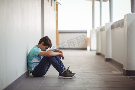 悲观情绪摄影照片_坐在走廊的哀伤的男小学生