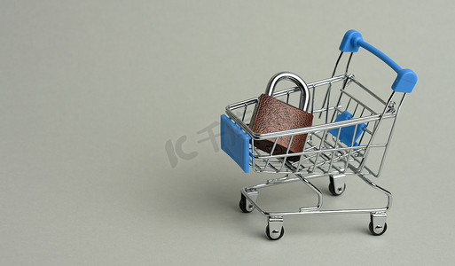 金属锁摄影照片_灰色背景上微型购物车中的金属锁。