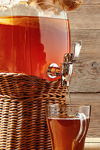 新鲜的自制康普茶发酵茶饮料装在带水龙头的罐子里，装在木制背景的杯子里。