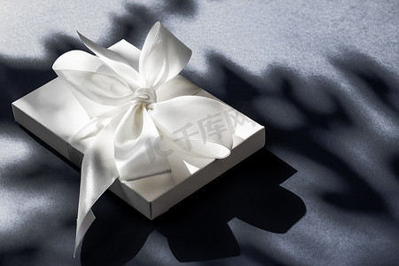 礼盒蝴蝶结摄影照片_黑色背景中带丝带和蝴蝶结的豪华假日白色礼盒、豪华婚礼或生日礼物