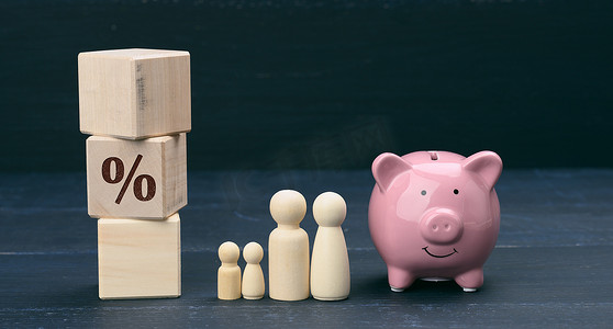 木制家庭小雕像和粉色陶瓷存钱罐，储蓄概念，预算控制