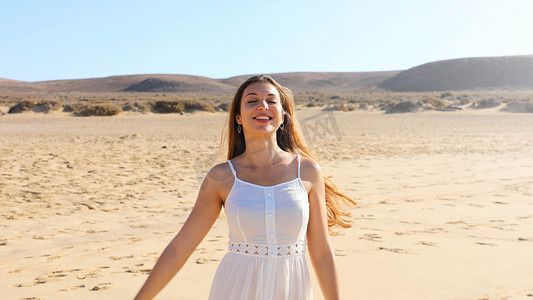 早上在加那利群岛兰萨罗特岛的沙滩上，穿着白色裙子跳舞呼吸新鲜空气的美丽年轻女子
