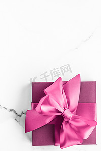 礼盒蝴蝶结摄影照片_大理石背景上带丝绸蝴蝶结的粉红色礼盒、女婴淋浴礼物和奢华美容品牌的魅力时尚礼物、假日平板艺术设计