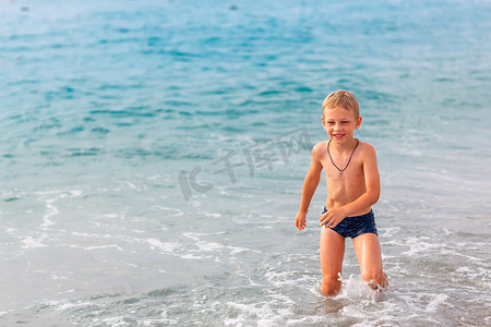 小男孩海边摄影照片_快乐的小男孩在海边的海浪中玩得开心