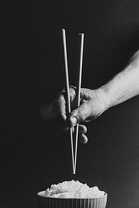 极简主义的老手在一碗米饭上抓着日本筷子，概念是在黑色和白色的黑色背景上用电影色调拍摄的