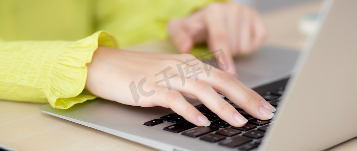 在家庭办公室的办公桌上使用笔记本电脑工作的手年轻亚洲女商人的特写，自由职业者在桌上的笔记本上看和打字，在线学习的女性，商业和教育概念。