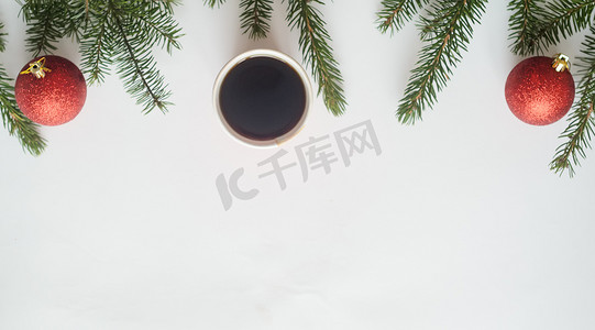 圣诞咖啡。顶视图、一杯咖啡和两个红球，白色背景上有圣诞树枝，下方有复制空间。