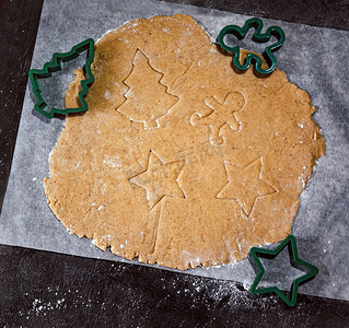 星星饼干摄影照片_在深色背景的羊皮纸烘焙纸上，以圣诞树、星星、小男人、生面团的形式切出姜饼饼干。