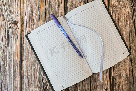 空白笔记摄影照片_用笔打开日记页，在木桌顶视图上做笔记