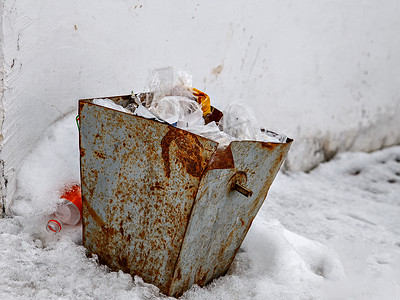 垃圾散落的容器靠墙立在雪地上