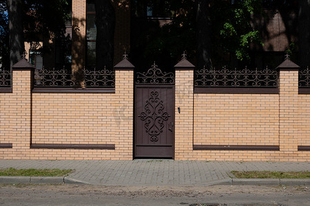 人行通道闸摄影照片_道路旁的浅棕色砖栅栏和锻铁门