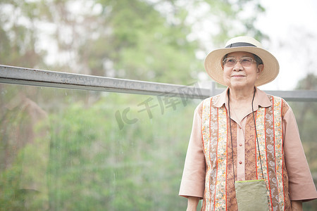 旅行的老人摄影照片_在公园的人行天桥上旅行的老年女性老年妇女旅行者。