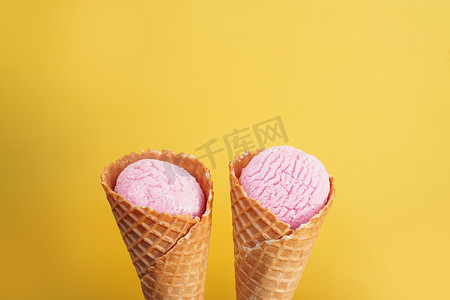 冰淇淋设计摄影照片_黄色背景中圆锥形的美味粉色冰淇淋。