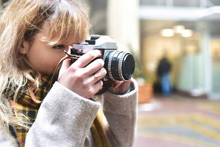 金发美女摄影师手里拿着复古相机，同时在城市旧建筑上拍照。