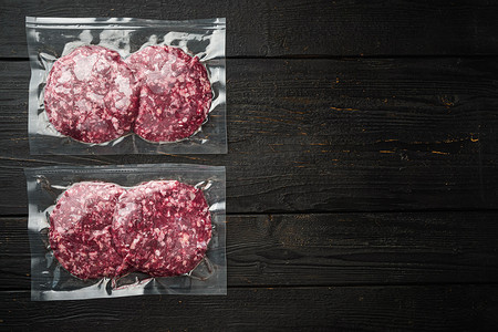 生鲜牛肉汉堡在塑料托盘中切碎肉，在黑色木桌背景上，顶视图平躺，带有文本复制空间