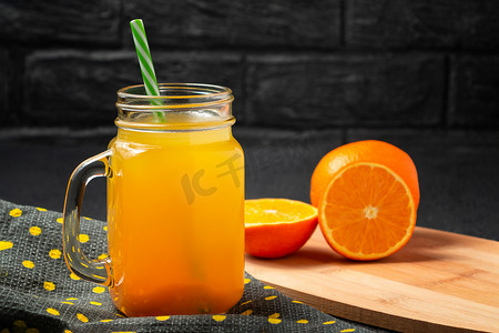 用橙子新鲜制作的柑橘汁，放在罐子里，杯子里放着灰色桌子上的吸管
