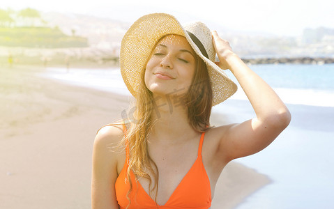 年轻开朗的比基尼女人戴着帽子在热带海滩上享受阳光。
