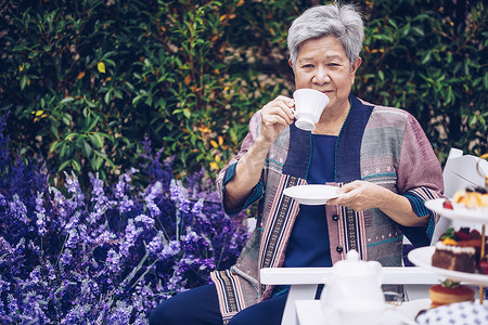 咖啡茶摄影照片_亚洲老年老年妇女在薰衣草花园里喝咖啡茶。