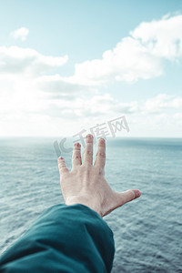 和平漫画摄影照片_一个男人的手越过清澈的海洋地平线，白云上有复制空间、灵感和自由概念