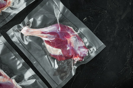 鸭腿摄影照片_密封袋中的生鸭腿肉，用于真空烹饪，黑石背景，顶视图平躺