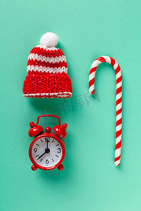 大气圣诞摄影照片_柔和的绿松石背景上的圣诞糖果手杖、时钟和帽子。