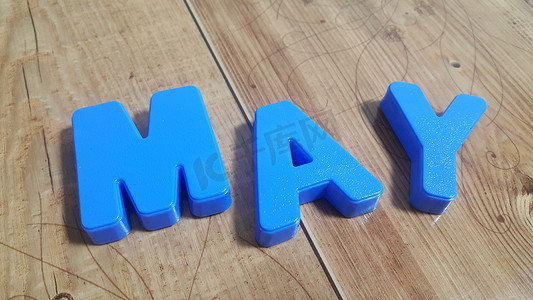 制作单词 May 的塑料彩色字母被放置在木地板上