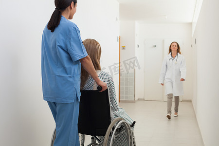 护士推着坐在轮椅上的病人，医生正在接近