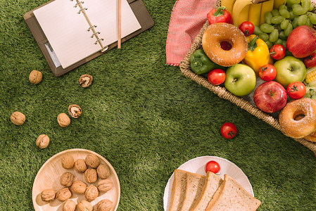 草地上的野餐毯上放着新鲜健康的热带水果，上面放着葡萄、苹果、葡萄柚、橙子和香蕉