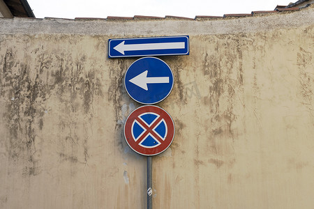 旧的蓝色金属箭头标志贴在损坏的混凝土墙上，指示向左走，没有停车标志