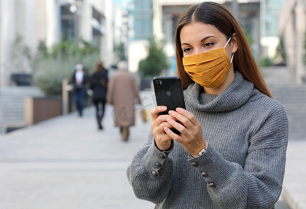 封锁开启时，戴着面罩坐在外面的年轻女性手持智能手机的画像
