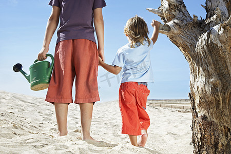 沙滩上枯树旁两个拿着水壶的男孩的后视