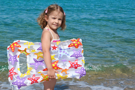 气垫摄影照片_站在海里的带气垫床的小女孩