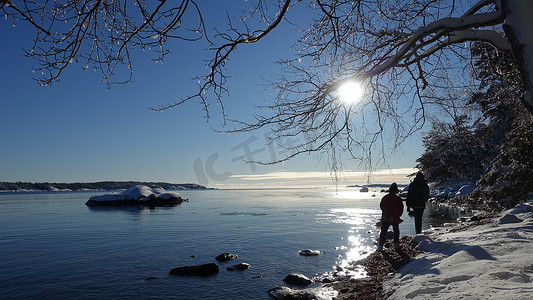 两个人在斯堪的纳维亚半岛的海边雪地和阳光充足的冬日散步