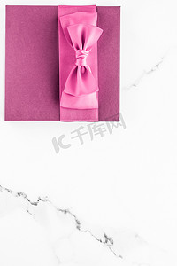 礼盒蝴蝶结摄影照片_大理石背景上带丝绸蝴蝶结的粉红色礼盒、女婴淋浴礼物和奢华美容品牌的魅力时尚礼物、假日平板艺术设计