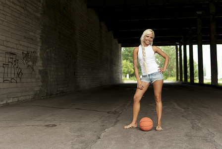 美丽的金发女孩站在街上打篮球
