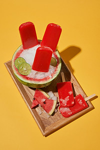 黄色背景下木盘上的夏日情调、西瓜冰棒和切片西瓜