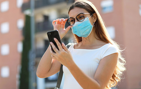 城市生活方式时尚潮人女孩戴着外科口罩在街上用手机阅读信息