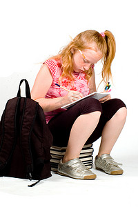 双肩包摄影照片_坐在一摞书上做作业的女学生
