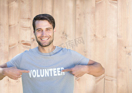 微笑的男人指着他 T 恤上的志愿者头衔