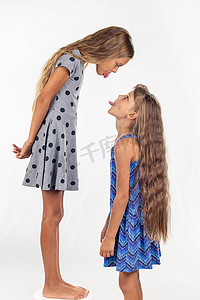 一个女孩站在椅子上，另一个女孩站在旁边，互相吐舌头