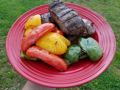 青椒牛肉摄影照片_手持红盘配烤牛排和红黄青椒