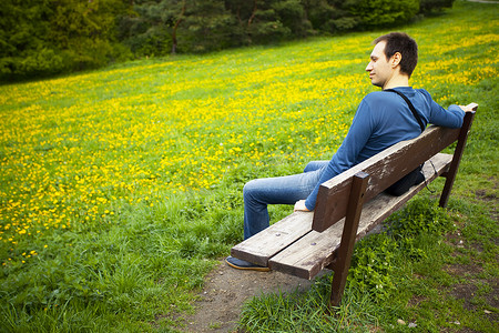 男性在蒲公英田的长凳上休息