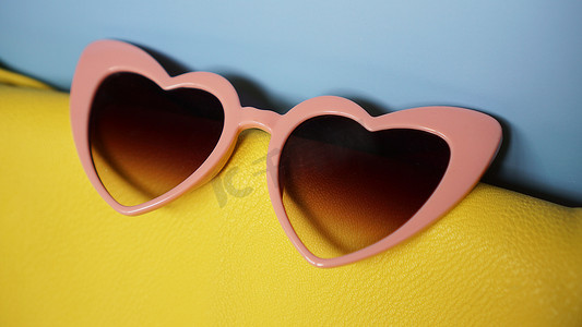 粉色夏天背景摄影照片_蓝色背景中的黄色包和心形太阳镜