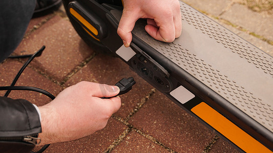 男子在特殊停车场用充电器为他的电动滑板车充电。