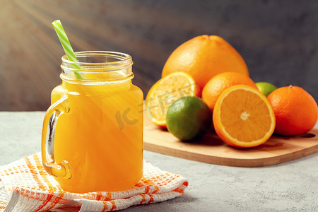 用橙子、葡萄柚和酸橙制成的新鲜柑橘汁放在一个罐子里，在灰色桌子上放着吸管