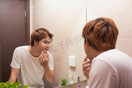 年轻的亚洲男人照镜子，在浴室里检查自己的皮肤