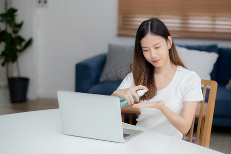 年轻的亚洲女性在家工作，使用酒精凝胶或消毒剂清洁手部，保护冠状病毒或 covid-19，新常态，检疫和社会疏远，女商人使用笔记本电脑。