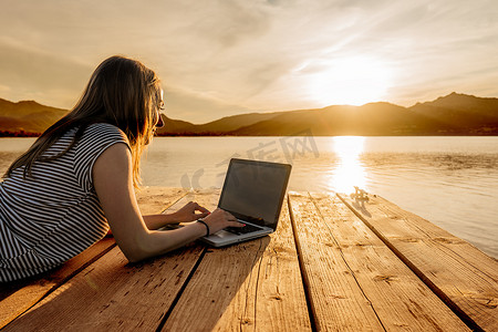 日落真实摄影照片_年轻女子在日落时在码头上享受她的创造力写书。