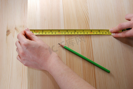 两只手用钢卷尺测量一块木板